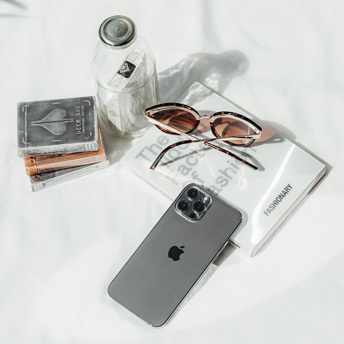 Smartphone, Sonnenbrille, Buch, Spielkarten und Flasche auf weißem Untergrund arrangiert.