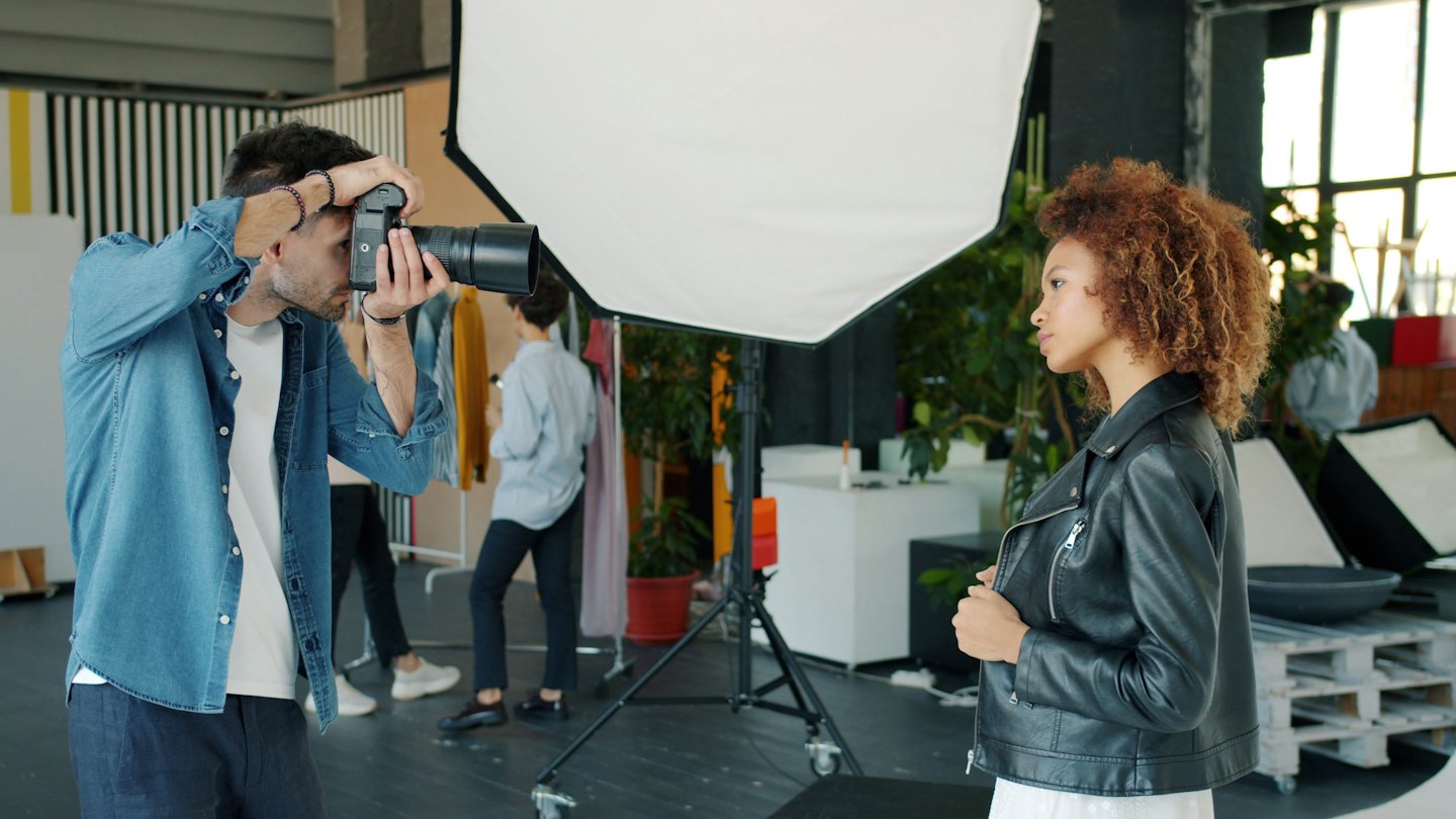 Fotograf richtet Kamera auf Model in hellem Studio.
