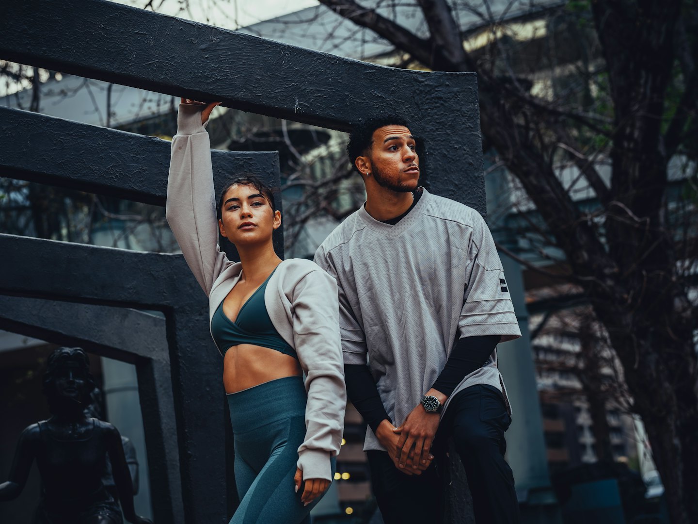Fitnessmodels posieren in Sportkleidung vor Betonstrukturen und kahlen Bäumen.